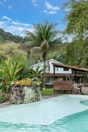 Ein Haus mit Schwimmbad, umgeben von üppiger Vegetation und blauem Himmel.