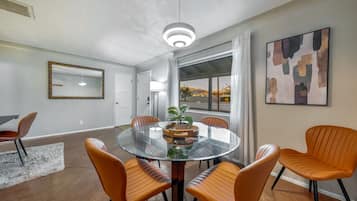 Uma sala de jantar moderna com uma mesa redonda de vidro, seis cadeiras laranja, um espelho grande e uma pintura contemporânea.