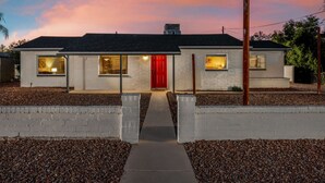 Ein zweistöckiges Haus mit roter Tür, einer kleinen angebauten Garage und einer Auffahrt zum Eingang.