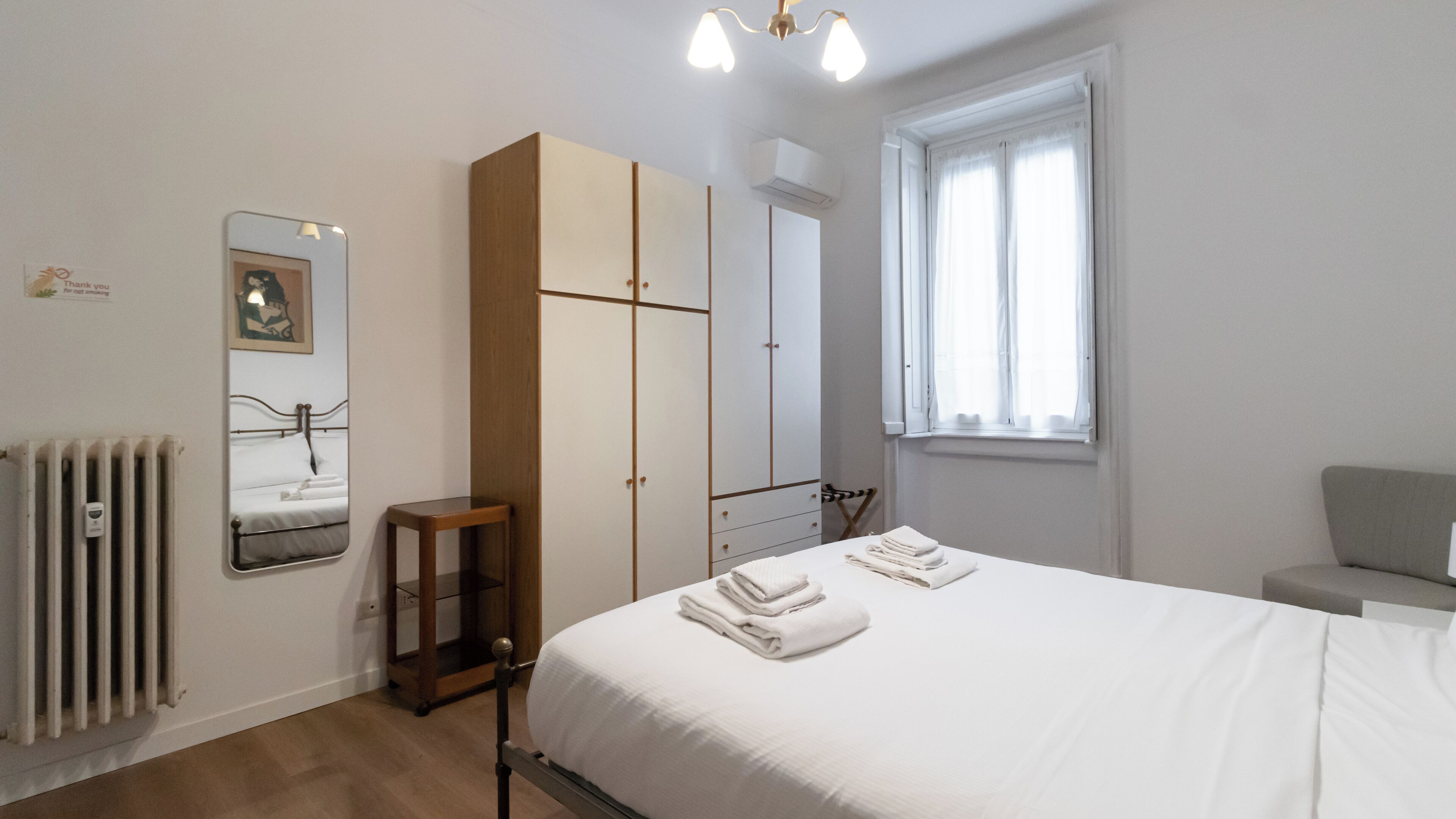 Un dormitorio con cama, armario, radiador, ventana y espejo.
