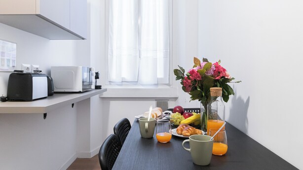 Eine moderne Küche mit Esstisch, gedeckt für das Frühstück, mit Croissants, Obst und Saft.