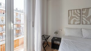 A bedroom with a bed, a nightstand, a lamp, and a view of a balcony with a building in the background. - Italianway Comfort - Negroli 11 (Milan)
