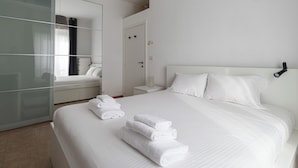 Ett hotellrum med en stor säng, ett sängbord, en liten avlastningsyta, en spegel och en garderob.