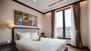 A hotel room with a large bed, a painting on the wall, a window with curtains, and a nightstand with a lamp. - CityHouse - Atelier Thao Dien (Ho Chi Minh City)
