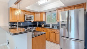 A modern kitchen with wooden cabinets, a stainless steel refrigerator, and a black countertop. - Seastars IV (Fort Myers Beach)