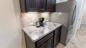 A kitchen with dark cabinets, a stainless steel refrigerator, and a marble countertop. - The Nest at Hackmatack (Houston)
