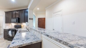 A kitchen with dark cabinets, a microwave, stove, and marble countertops. - The Nest at Hackmatack (Houston)