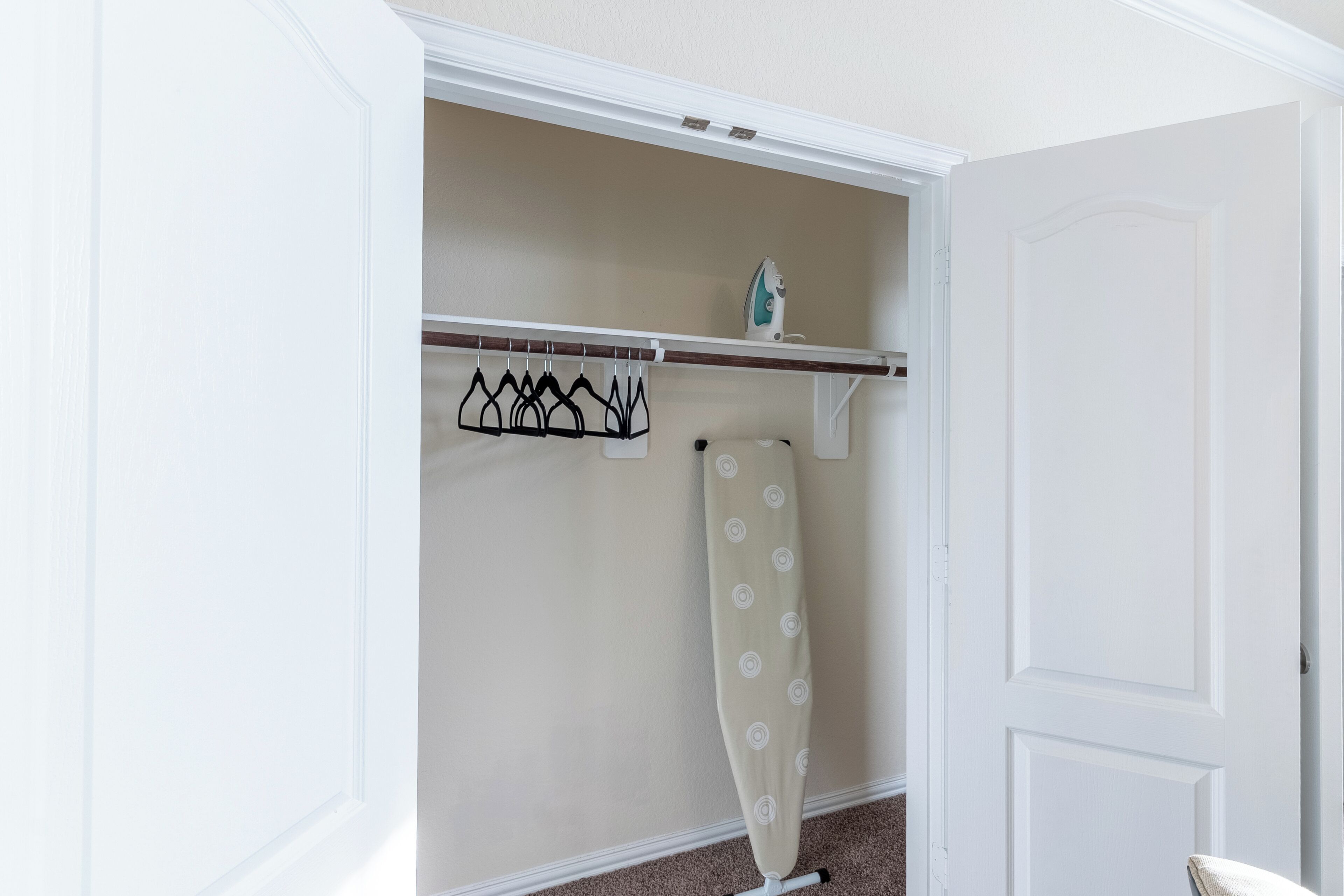 Un dressing avec une tringle pour suspendre les vêtements, une tringle pour le rideau de douche et une petite étagère avec un fer à repasser.