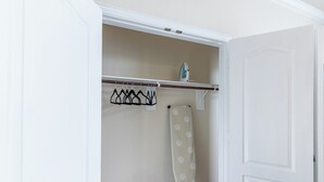 A walk-in closet with a hanging rod, a shower curtain rod, and a small shelf with an iron. - The Nest at Hackmatack (Houston)
