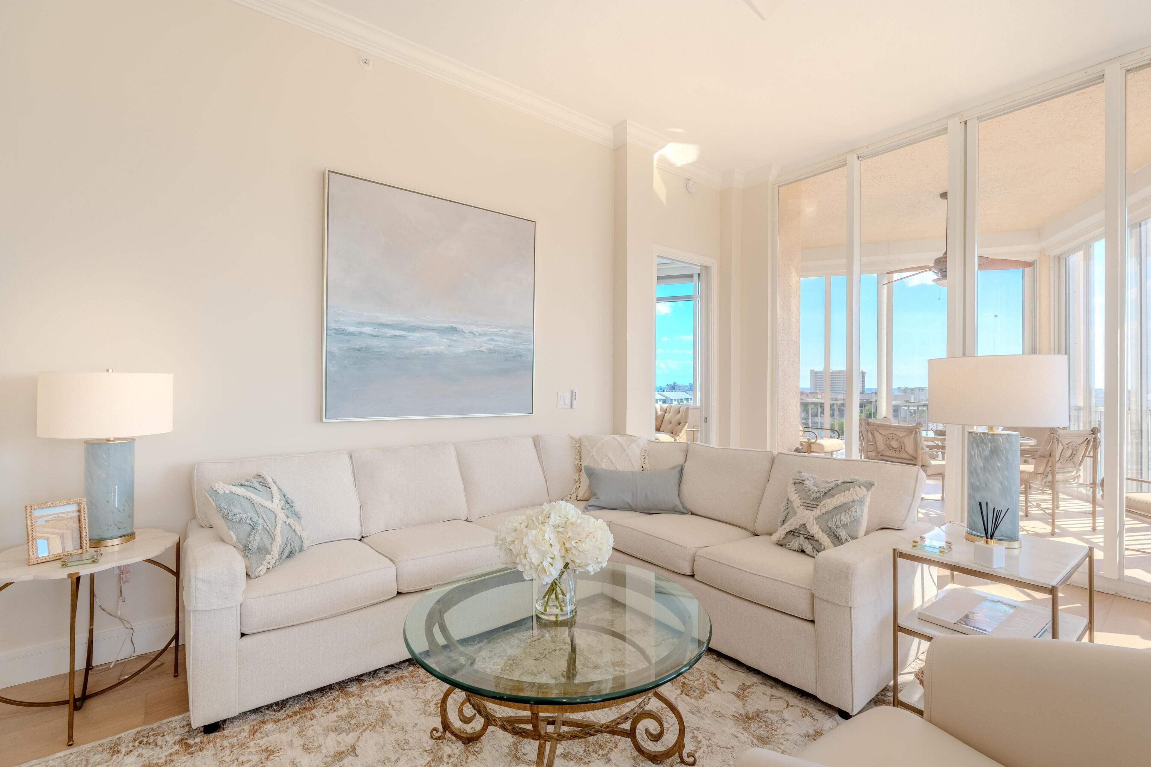 A spacious living room with a large window, a glass coffee table, and a beige sofa.