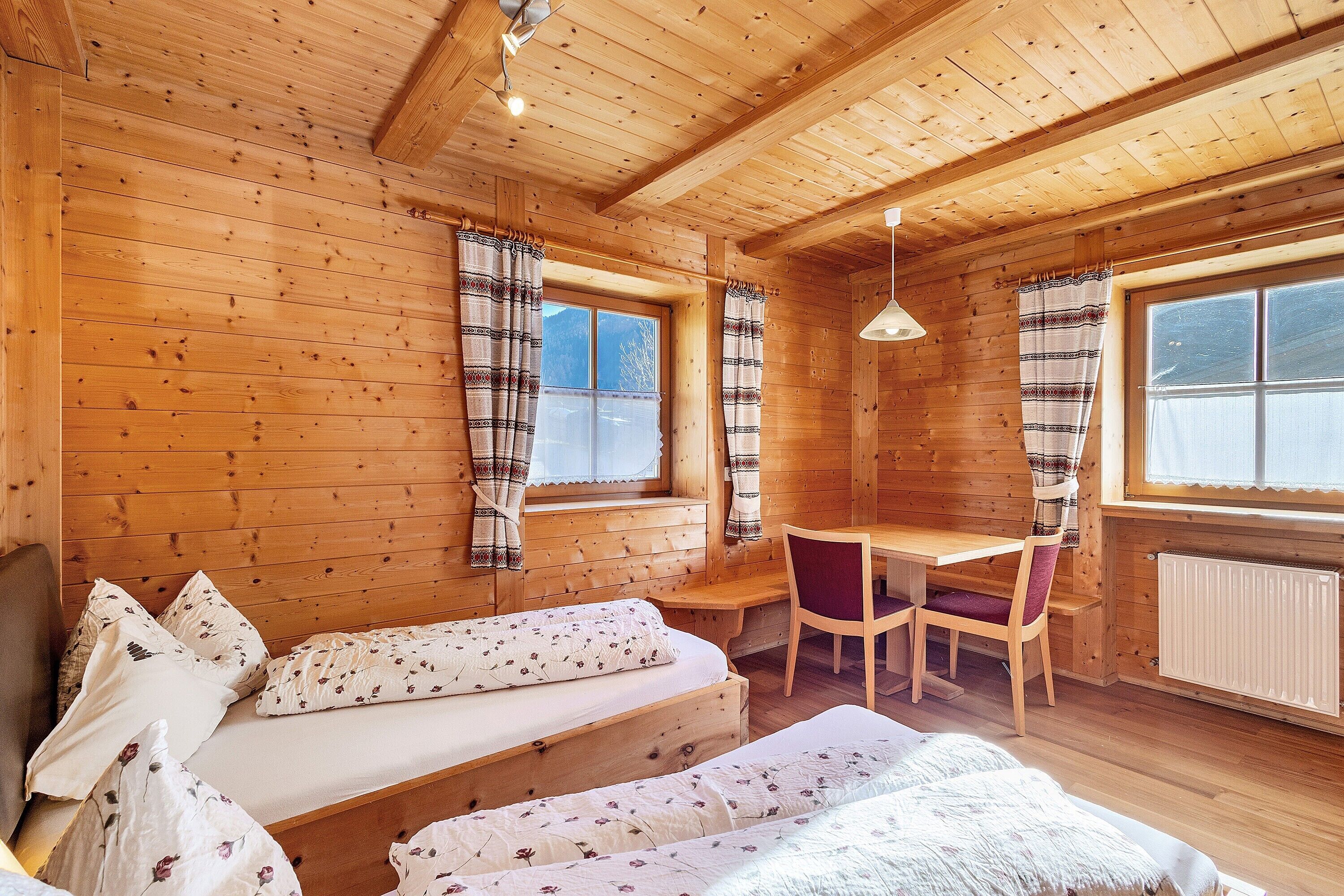 A wooden cabin room with a bed, a table, and a chair.