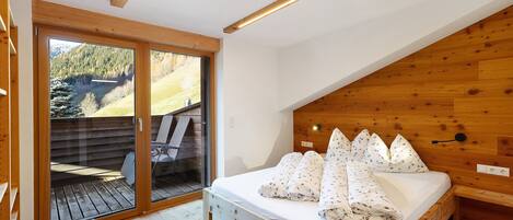 Un dormitorio con cama, cabecera de madera y vista a una terraza exterior a través de un ventanal.