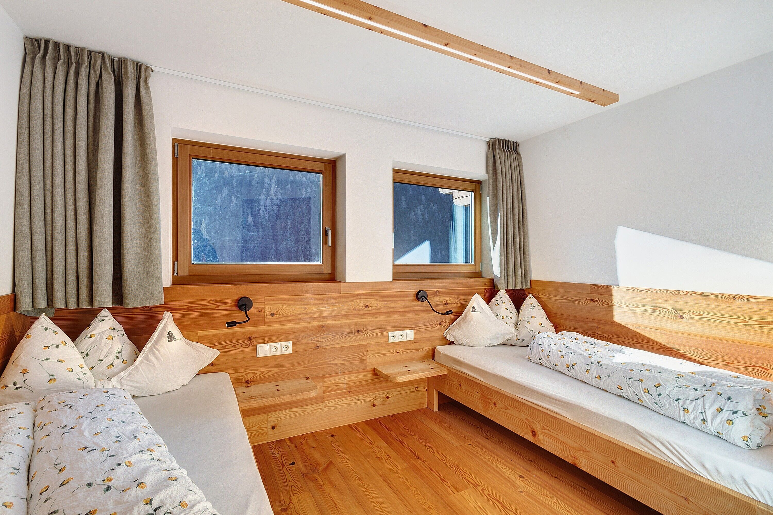 Une chambre avec deux lits en bois, une fenêtre et une tête de lit en bois.