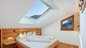 Une chambre avec un puits de lumière, une tête de lit en bois, un lit avec une literie blanche, une table de chevet et un petit banc en bois.