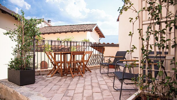 Eine Terrasse mit Tisch und Stühlen, einem Blumentopf und Blick auf ein Gebäude mit Ziegeldach.