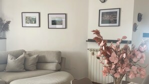 Ein Wohnzimmer mit einer Couch, einem Esstisch mit gemustertem Tischläufer und einer Vase mit Blumen.