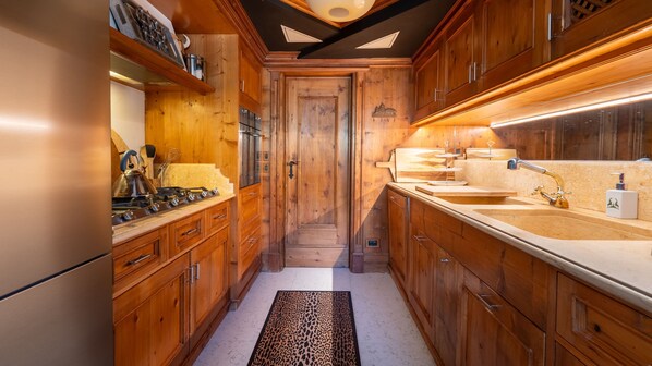 A narrow kitchen with wooden cabinets, a stainless steel refrigerator, and a countertop with a sink and faucet.