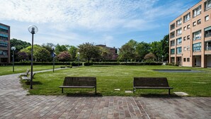 A park with two benches, a paved walkway, and a building in the background. - Bedetti Modern Flat by Wonderful Italy (Bologna)