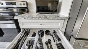 Una cocina con microondas, horno y un cajón con utensilios.