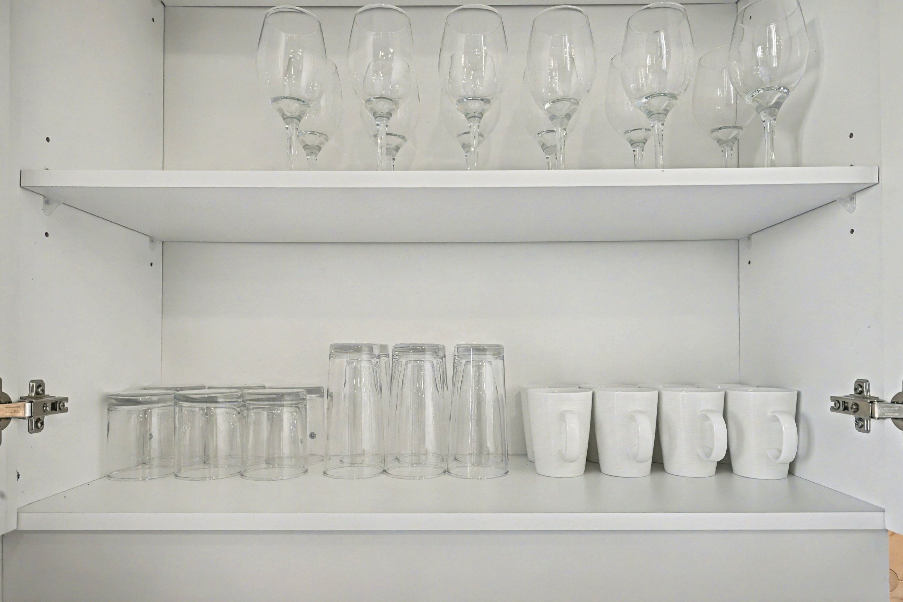 A white shelf with wine glasses and clear mugs.