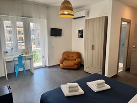 Una moderna camera d'albergo con un letto, una scrivania, una sedia, un armadio e una TV appesa al muro.