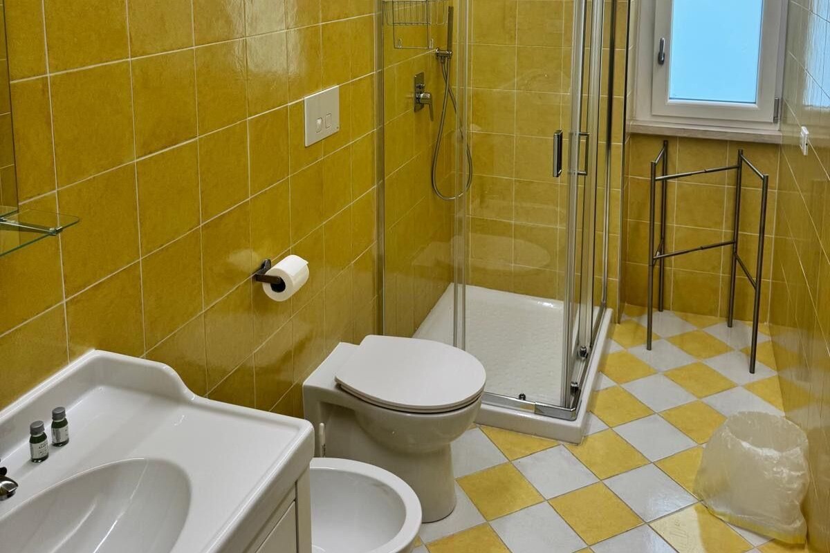 A bathroom with yellow tiles, a glass shower enclosure, a toilet, and a sink with a mirror.