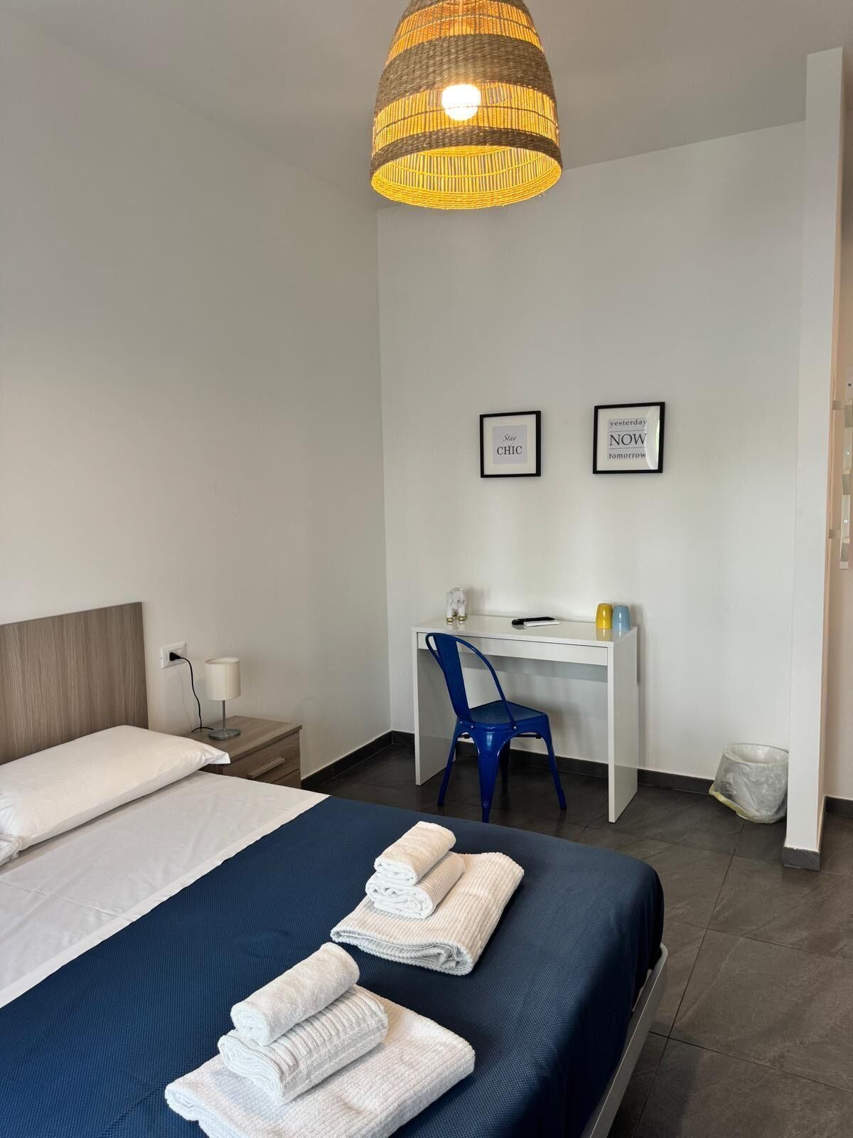 Une chambre d’hôtel avec un lit, un bureau et une chaise. Deux tableaux encadrés sont accrochés au mur.