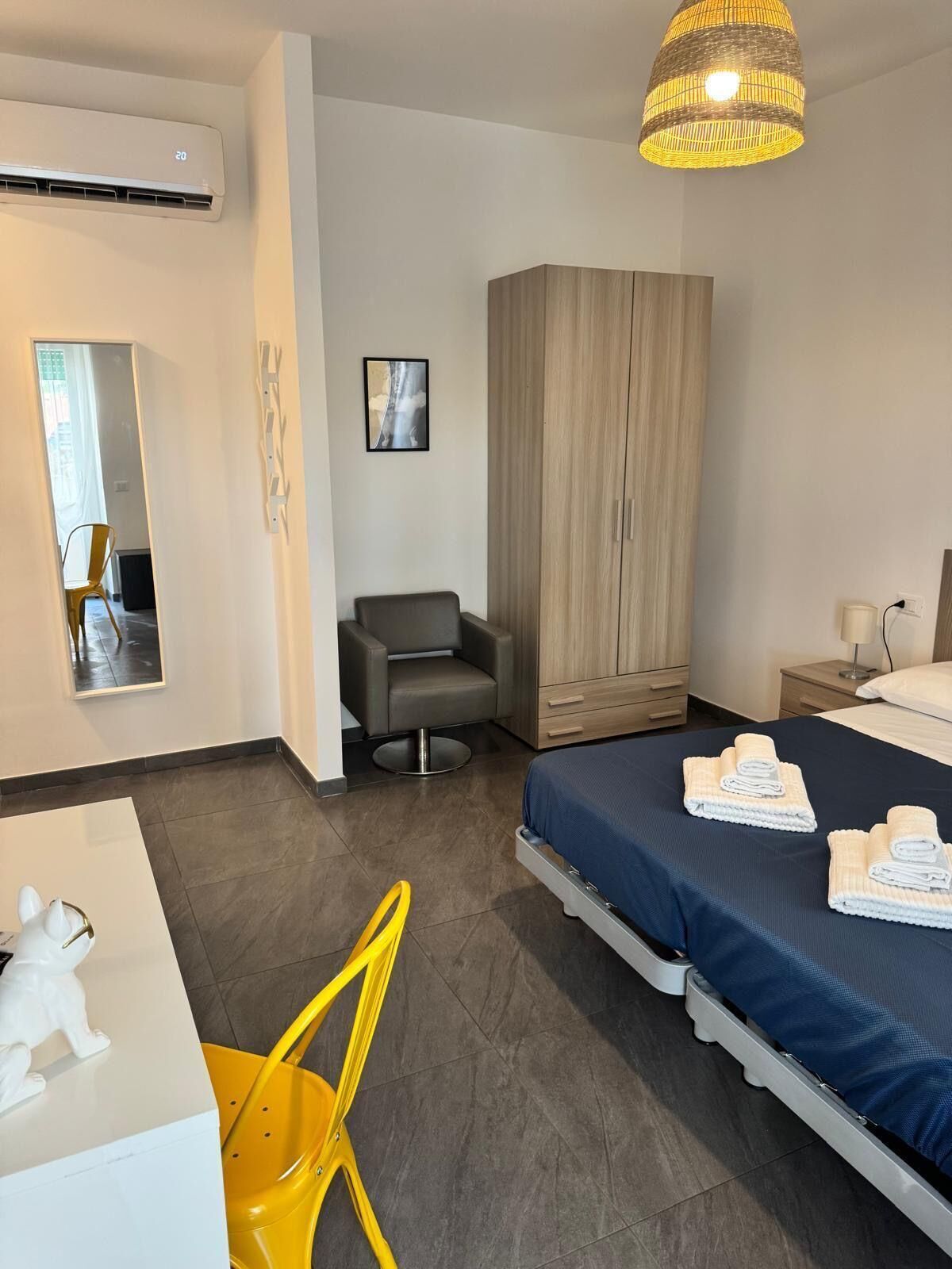 Una moderna camera d'albergo con un letto, una scrivania, una sedia, un armadio e una lampada a sospensione.