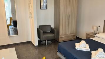 Una moderna camera d'albergo con un letto, una scrivania, una sedia, un armadio e una lampada a sospensione.