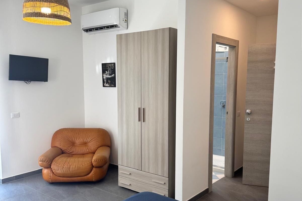 A modern bedroom with a bed, a chair, a wardrobe, and a TV.