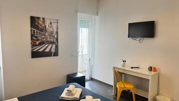 A hotel room with a bed, a desk, a chair, a TV, and a painting on the wall.