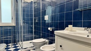 A bathroom with blue tiles, a glass shower enclosure, a white toilet, a bidet, and a white sink with a mirror. - Sapore Di Mare Riviera (Gaeta)