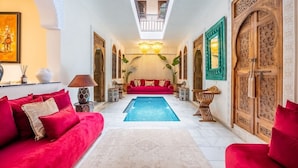 A luxurious living room with a pool, red sofas, and ornate wooden doors. - Riad Dar Lghizlane (Marrakech)