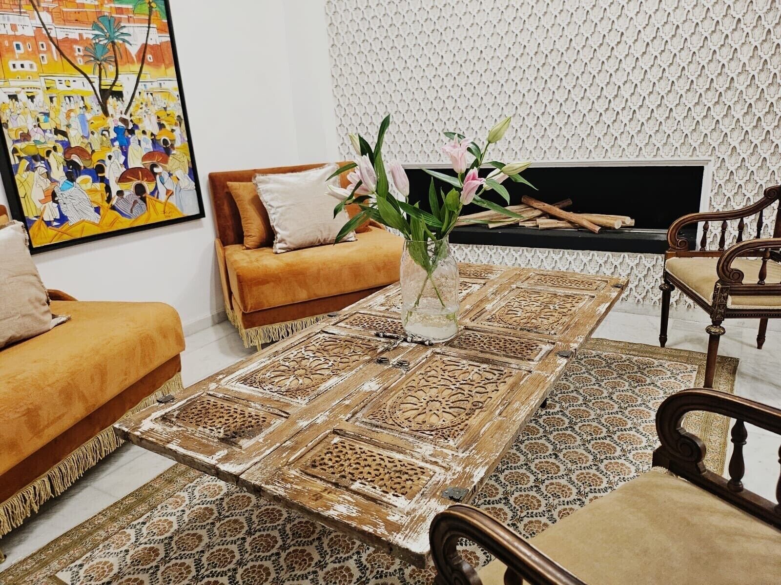 Una sala de estar con un sofá, una mesa de centro con diseños intrincados, un jarrón con flores y una chimenea.