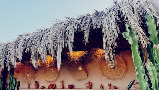 A thatched-roof outdoor seating area with cushions and a variety of decorative pots and vases. - Riad Dar Lghizlane (Marrakech)