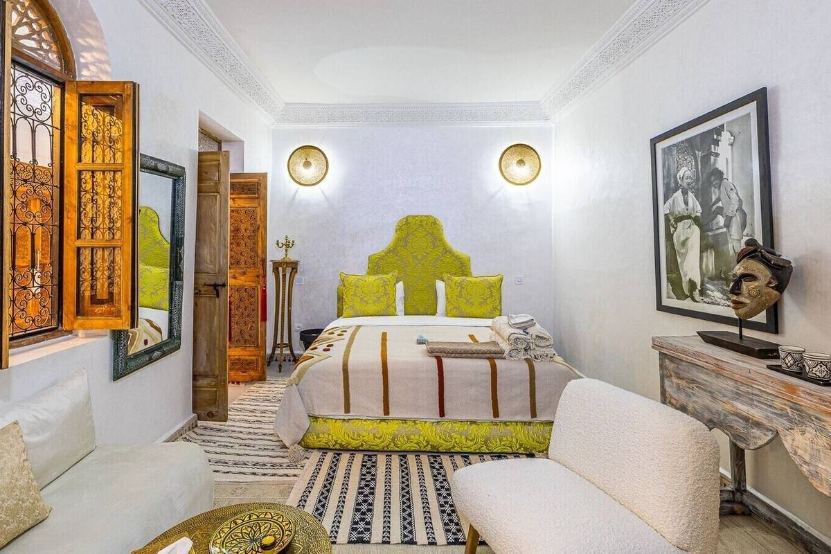 A bedroom with a large bed, a sofa, a side table, and a wall-mounted shelf.
