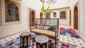 A traditional interior with a wooden bench, two ornate tables, and patterned rugs. - Riad Dar Lghizlane (Marrakech)