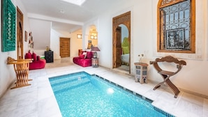 A spacious indoor pool area with a tiled floor, a red sofa, and a wooden bench. - Riad Dar Lghizlane (Marrakech)