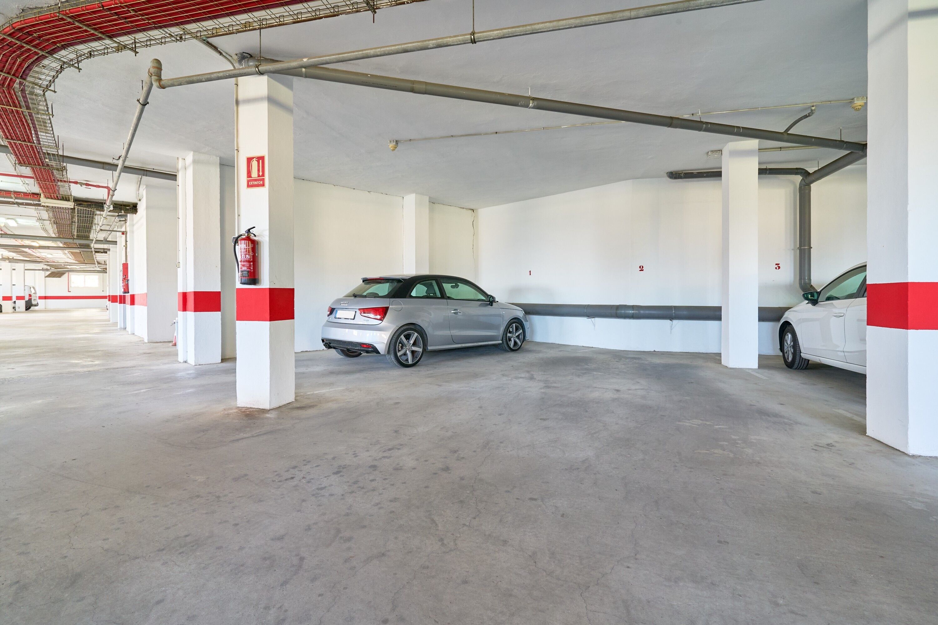 A parking garage with concrete floors, white pillars with red stripes, and fire extinguishers.