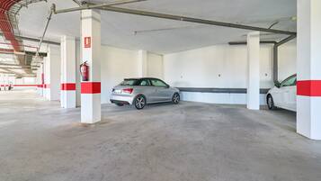 A parking garage with concrete floors, white pillars with red stripes, and fire extinguishers.