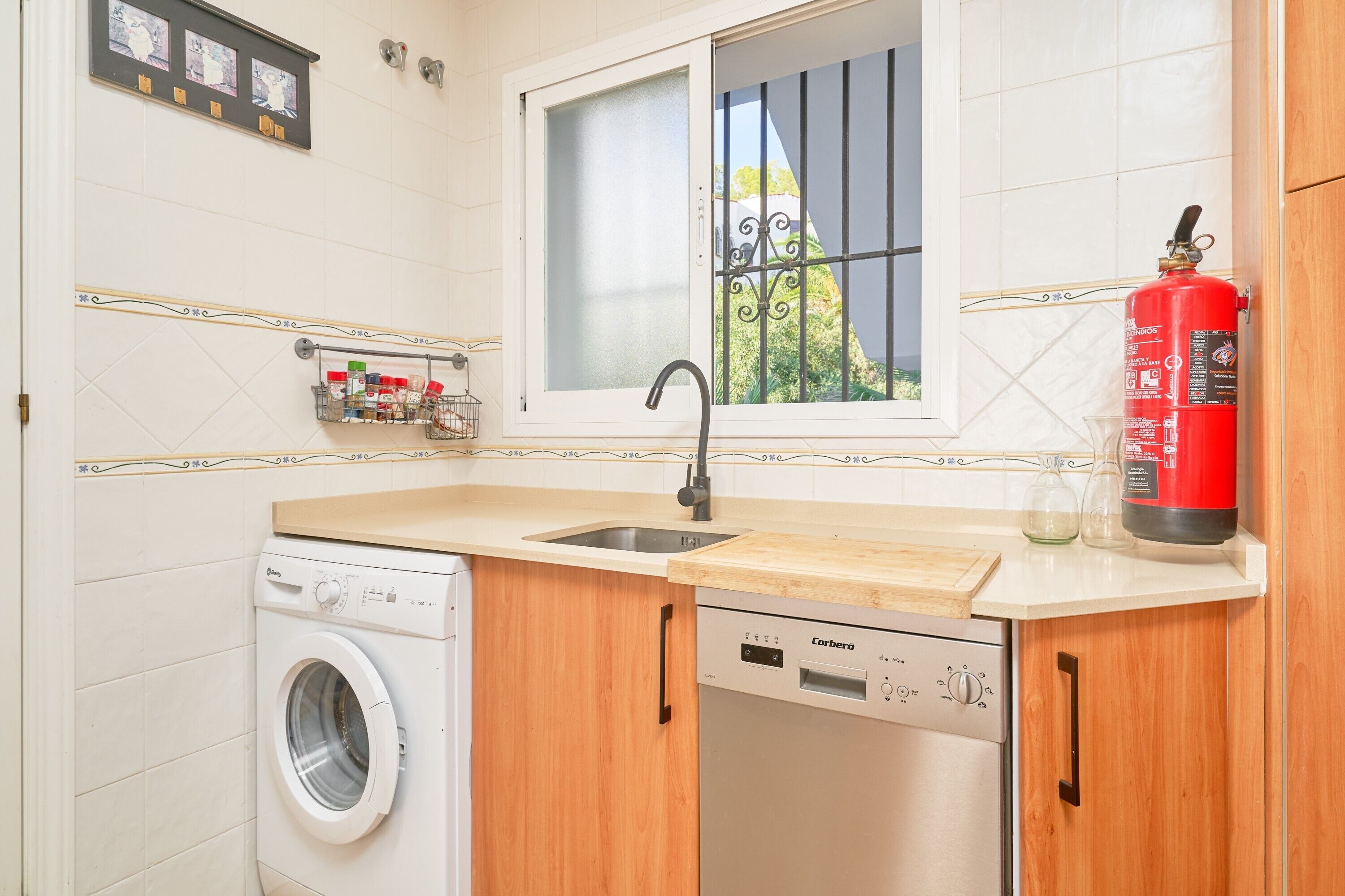 A kitchen with a washing machine, dishwasher, and a fire extinguisher.