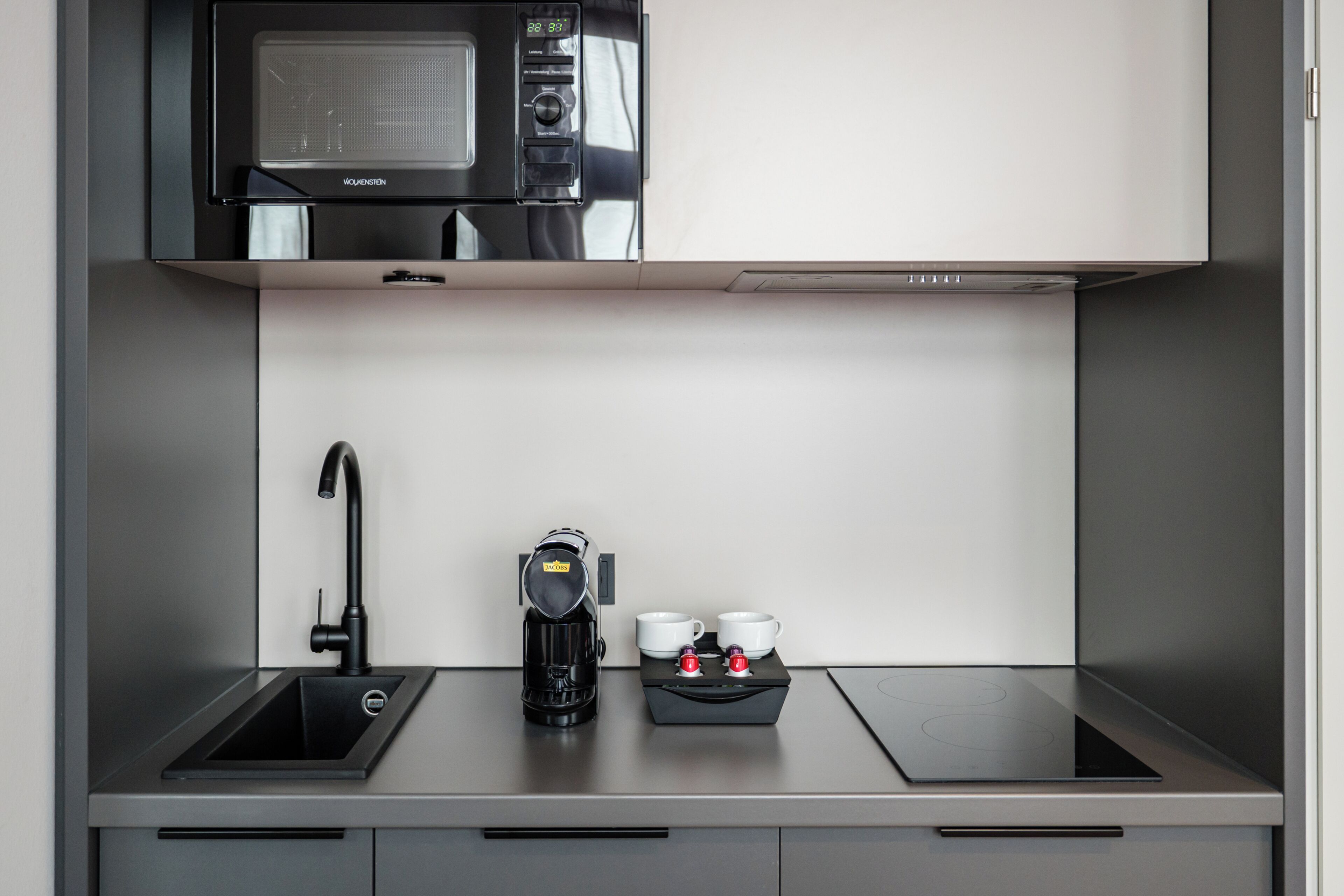 Une cuisine moderne équipée d’un four à micro-ondes, d’une machine à café et de deux tasses.