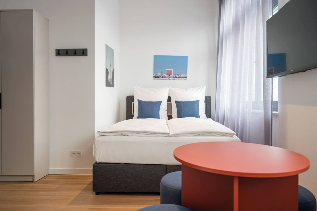 A modern bedroom with a bed, a red table, and a cityscape picture on the wall.