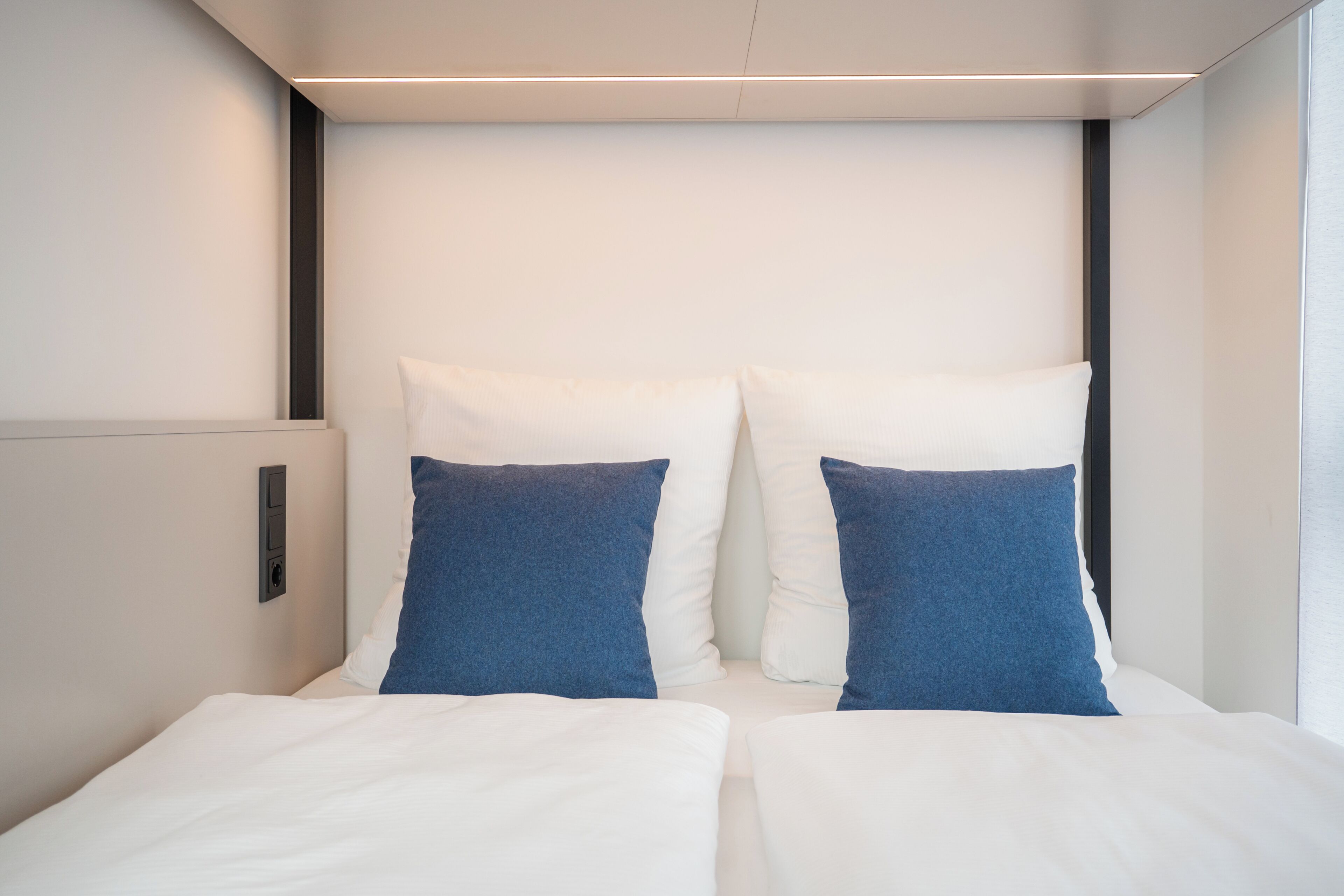 Une chambre d’hôtel moderne avec un grand lit, deux oreillers, une table de chevet et un panneau de commande fixé au mur.