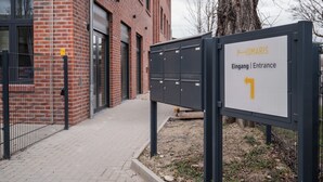Une entrée d’immeuble avec une pancarte indiquant « Eingang | Entrance » et une flèche indiquant la direction.