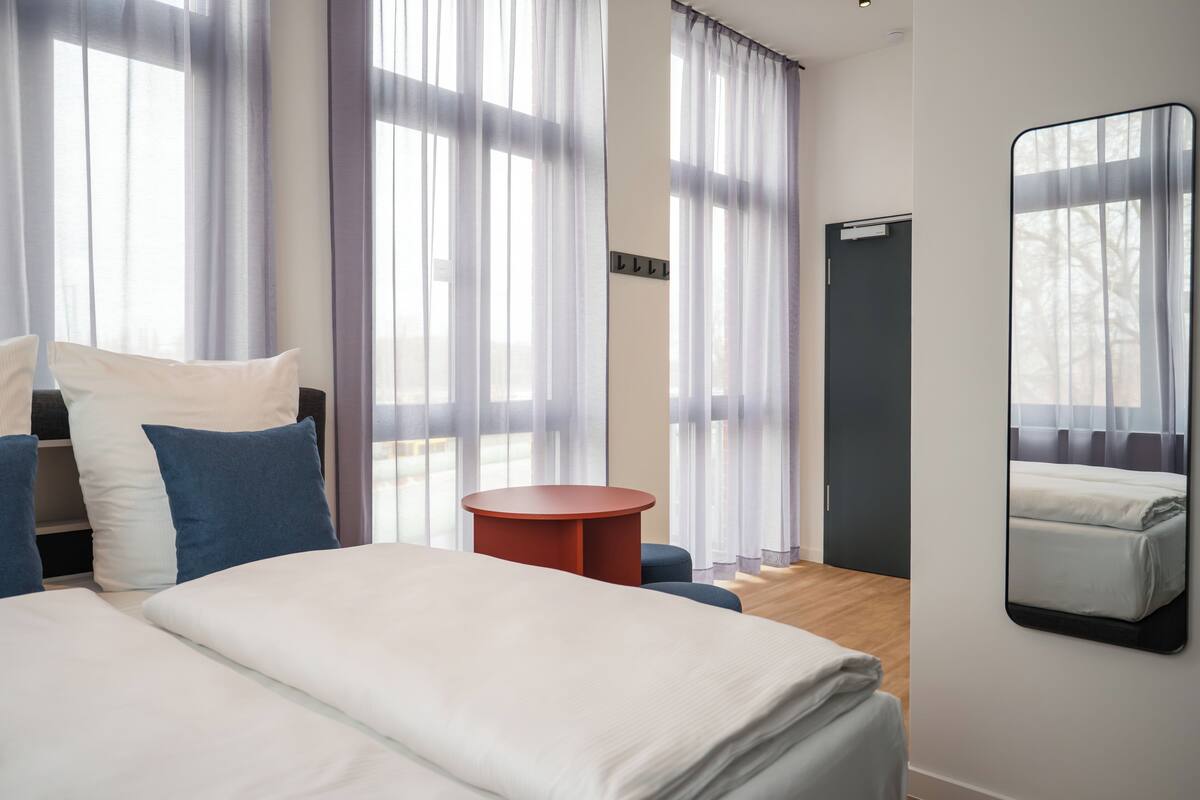A hotel room with a bed, a round table, and a large mirror.