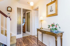 A hallway with a wooden staircase, a decorative table with a vase of flowers, and a framed picture on the wall. - Toast Stays - Elgin Escape (Darlington)