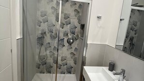 A modern bathroom with a glass shower enclosure, a wooden floor, and a white sink with a mirror. - Pertichetti Living room 2 (Foligno)