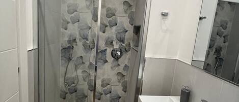 A modern bathroom with a glass shower enclosure, a wooden floor, and a white sink with a mirror.