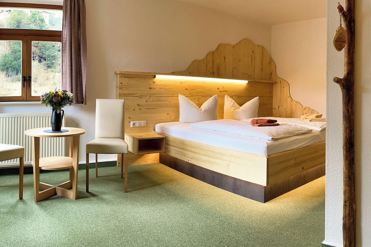 A wooden bed with a headboard, a bedside table, a chair, and a small table with a vase of flowers.